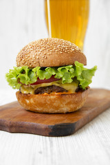 Cheeseburger and glass of beer on wooden board on white wooden background, side view. Close-up.
