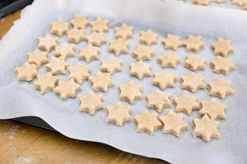 Home baking Christmas cookies: star shaped biscuits arranged on baking sheet with paper