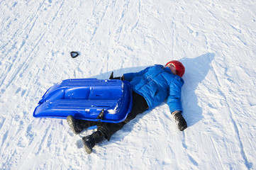Child boy crashed on a bobsled. Having fun on the snow. Children winter activities.