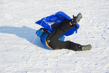 Fototapeta na wymiar Child boy crashed on a bobsled. Having fun on the snow. Children winter activities.