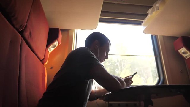 man silhouette travel is sitting on the train carriage holding sits by the window a smartphone Railway in headphones. slow motion video. man writes messages in the smartphone in lifestyle the train