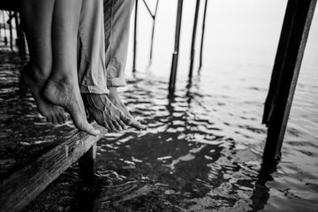 Feet of a couple in love sitting on the bridge looking at the sea while their legs are rolling waves