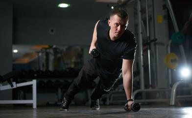 Fototapeta na wymiar Man doing push-up exercise with dumbbell. Workout Exercise. Sporty Athletic Male Exercising in a gym room 