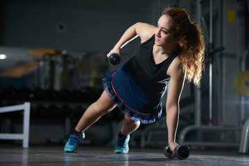 Fototapeta na wymiar Young woman doing push-up exercise with dumbbell. Workout Exercise. Sporty Athletic Girl Exercising in a gym room 