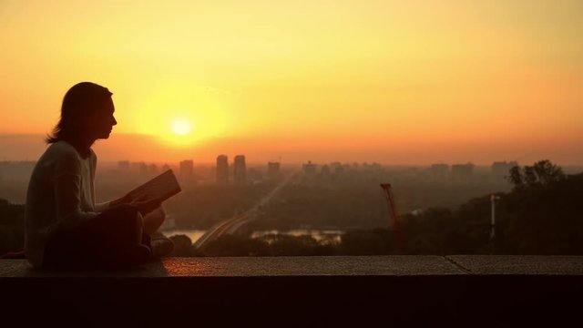 lady observes the city while holding the book. stunning sundown over the town.