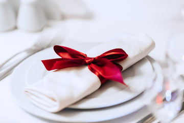 Close-up of a white napkin with a beautiful red bow on the plate