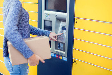 Woman using automated self service post terminal machine or locker to deposit the parcel for storage