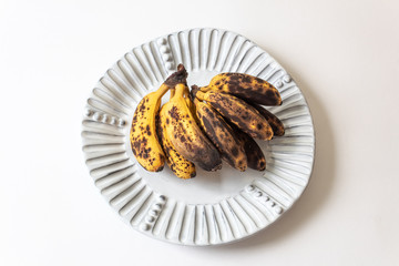Overripe baby bananas on a fluted white plate, isolated on white, horizontal aspect