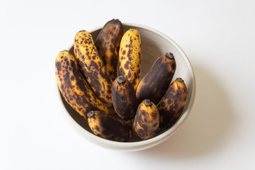 Small bowl of overripe baby bananas, isolated on white, horizontal aspect