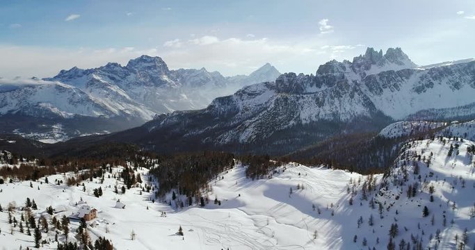 Backward aerial to snowy alpine valley with woods forest at Cinque Torri.Sunny sunset or sunrise,sunny day,cloudy sky.Winter Dolomites Italian Alps mountains outdoor nature establisher.4k drone flight