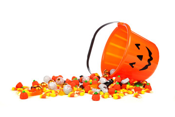 Spilling Halloween Jack o Lantern candy collector with a pile of candy over a white background