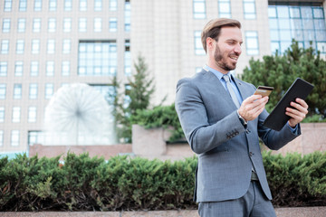 Handsome young businessman making an online purchase on a tablet while standing in front of an office building. Stay connected anywhere concept