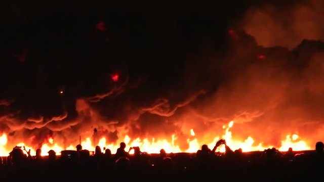 A pyrotechnic wall of fire explodes in front of the audience at the end of an air show.