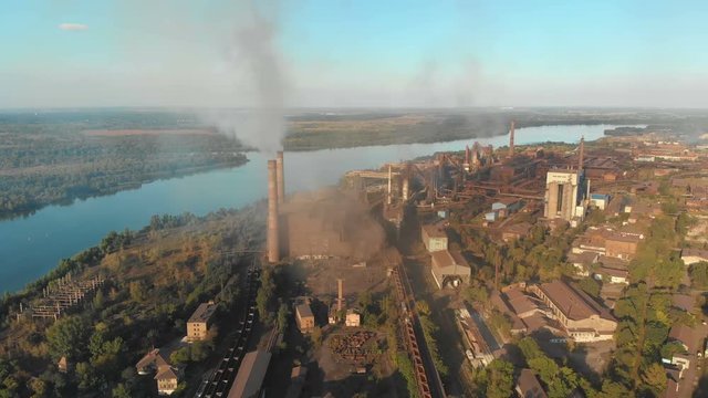 Aerial view of the Industrial Plant with Smoking Pipes near the City. Industrial zone. View from the drone to the Metallurgical factory near the river. Poor environmental conditions of the environment