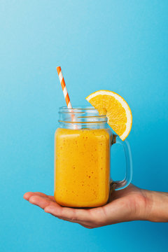Freshly prepared smoothies from ripe orange in hand on a blue background, close-up