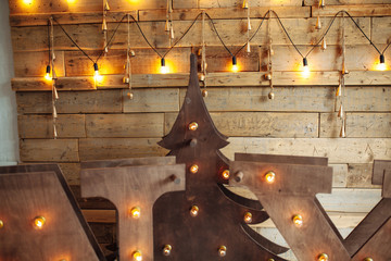 Alternative wooden christmas tree. A handmade New Year tree with light bulb on the floor on wooden background. Loft interior. Copy space