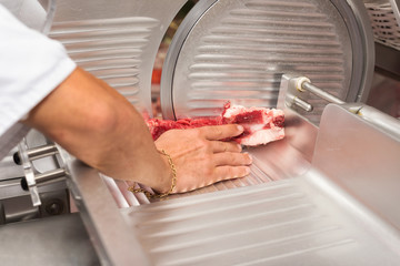 hand of butcher using slicer in butcher shop