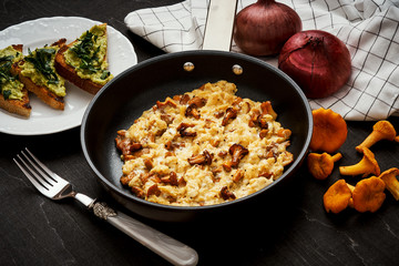 delicious scrambled eggs with chanterelles straight from the forest in a pan and bread with avocado on a wooden kitchen table