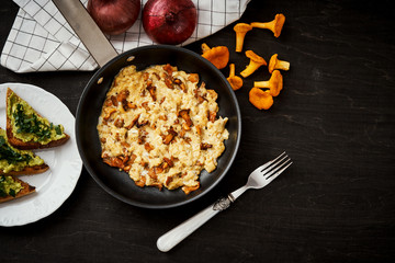 delicious scrambled eggs with chanterelles straight from the forest in a pan and bread with avocado on a wooden kitchen table