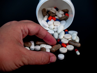 A person holding pills of different sizes, shapes and colors with his hand. Health concept