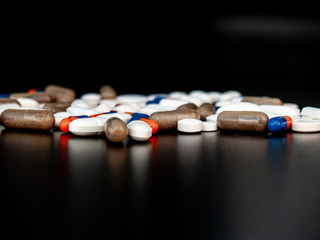 Pills of different sizes, shapes and colors with black background. Health concept