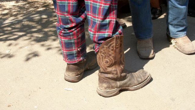 Feet and legs of two kids in cowboy boots, one in pajama pants, at the livestock barn at a county fair.