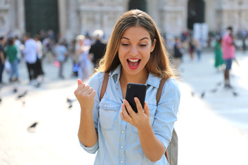Euphoric happy winner woman watching very good news on her smart phone in square