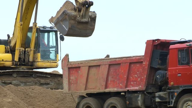 The excavator loads the sand with a large bucket into the lorry. Road construction