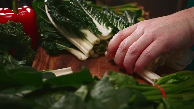 Woman's hands cut silverbeet spinach leaves on wooden cutting board in kitchen preparing healthy food