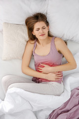 Young woman suffering from abdominal pain in bedroom