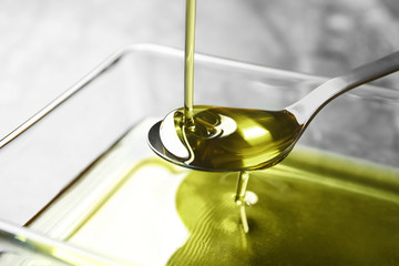 Pouring hemp oil into spoon over glass bowl, closeup