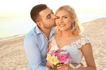 Groom hugging and kissing bride on beach. Wedding couple