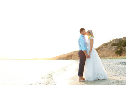 Wedding couple holding hands and kissing on beach. Space for text