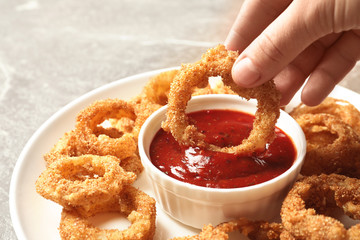 Woman dipping crunchy fried onion ring in tomato sauce, closeup