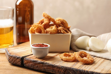 Cardboard box with crunchy fried onion rings and sauce on table