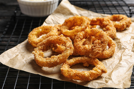 Cooling rack with homemade crunchy fried onion rings on wooden background, closeup