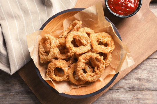 Homemade crunchy fried onion rings in plate and sauce on wooden background, top view