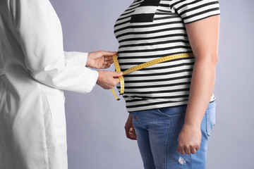 Doctor measuring fat woman's waist on grey background. Weight loss