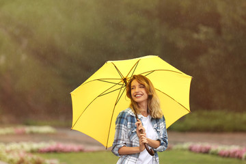 Happy young woman with umbrella under rain in park