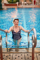 adult Woman with short hair In Fashion Swimwear Coming Out From Swimming Pool blue Water in hotel. vacation concept