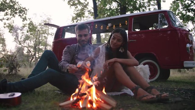 Beautiful young couple roasting marshmallows over a campfire while enjoying their road travel, slow motion