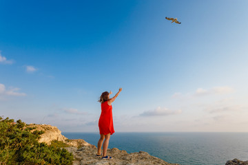 A girl walking over the sea on a cliff at sunset, draws her hands to a seagull flying in the clear sky. Catch a bird.Horizontal  banner for website header design with copy space for text.
