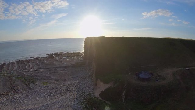 A rising aerial crane drone shot of nash cove at sunset with a film set below and the atlantic ocean in shot. would make a great establishing shot.