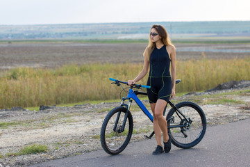 Fototapeta na wymiar A girl riding a mountain bike on an asphalt road, beautiful portrait of a cyclist at sunset 