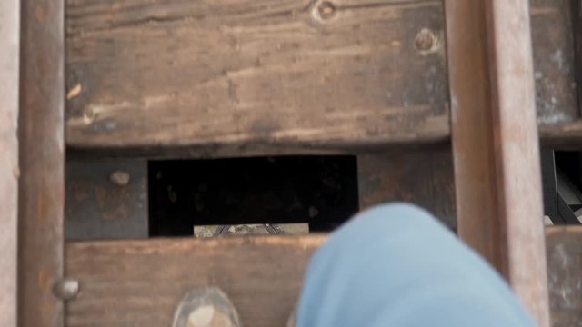 Man walks over train trestle while looking down into ravine through railway rails and ties.