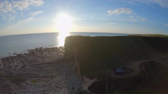 A panning/crabbing aerial drone shot of nash cove at sunset with a film set below and the atlantic ocean in shot. would make a great establishing shot.