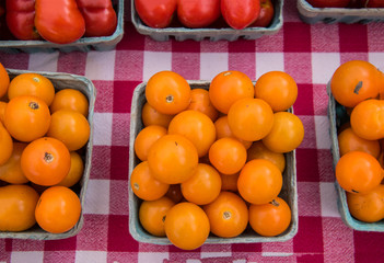 Quart of round orange cherry tomatoes on a checkerboard red and white tablecloth