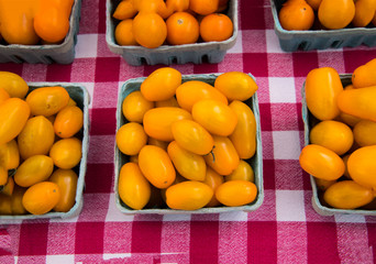 Quart of small fresh yellow tomatoes on a red and white checkered tablecloth