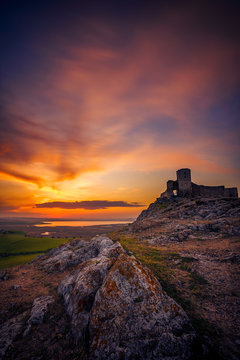Old ruined citadel on a rocky hill shot at sunset with some rocks in the foreground with dramatic long exposure clouds