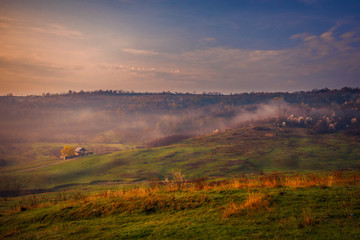 Beautiful morning landscape scene in the village with an isolated house in the background and some fog